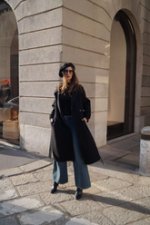 a lady in a black top, a black long wool coat and a pair of wide leg jeans